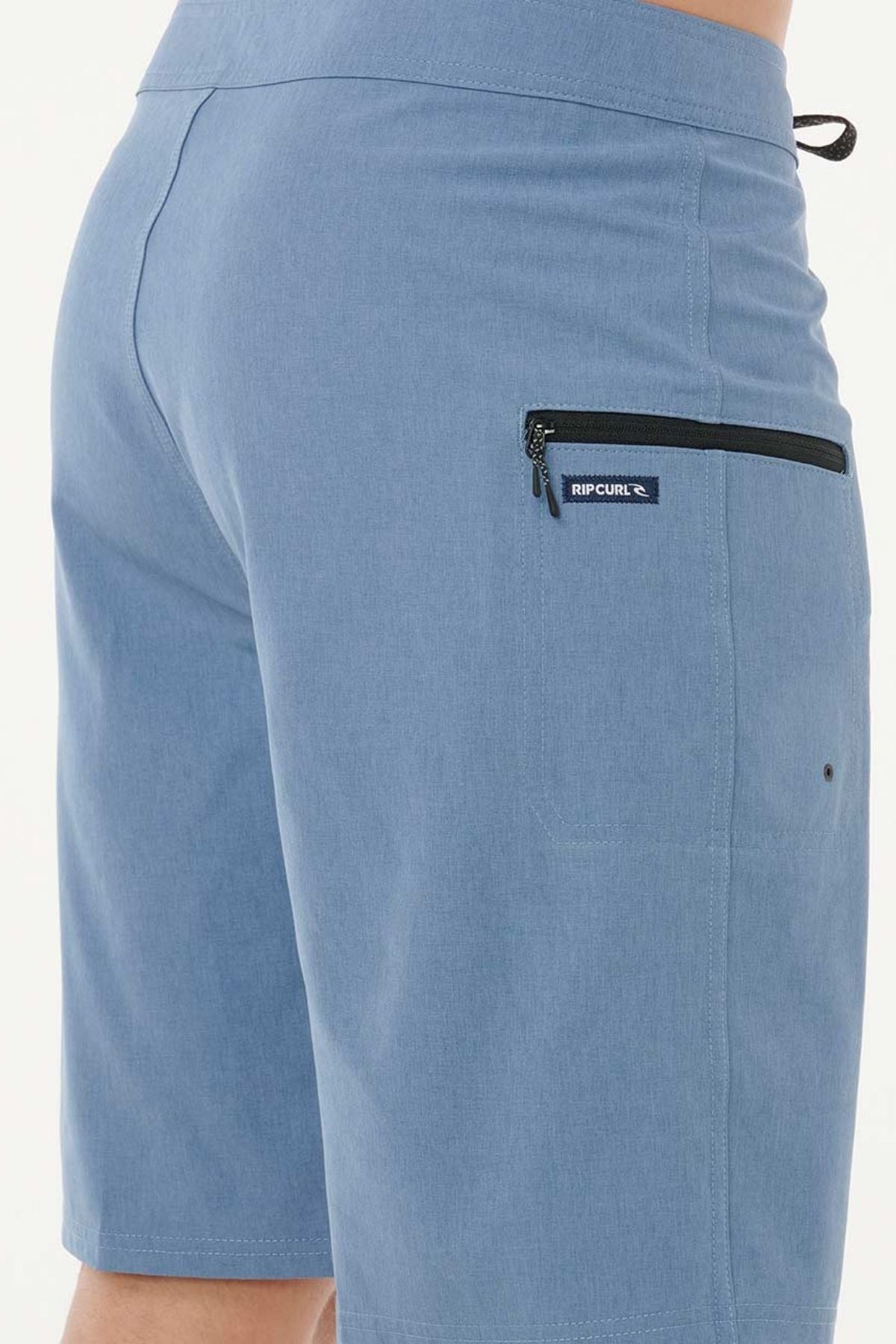 A close-up of a person wearing Rip Curl Mirage Core Boardshort, highlighting the back pocket with a black zipper and the signature Rip Curl logo tag.