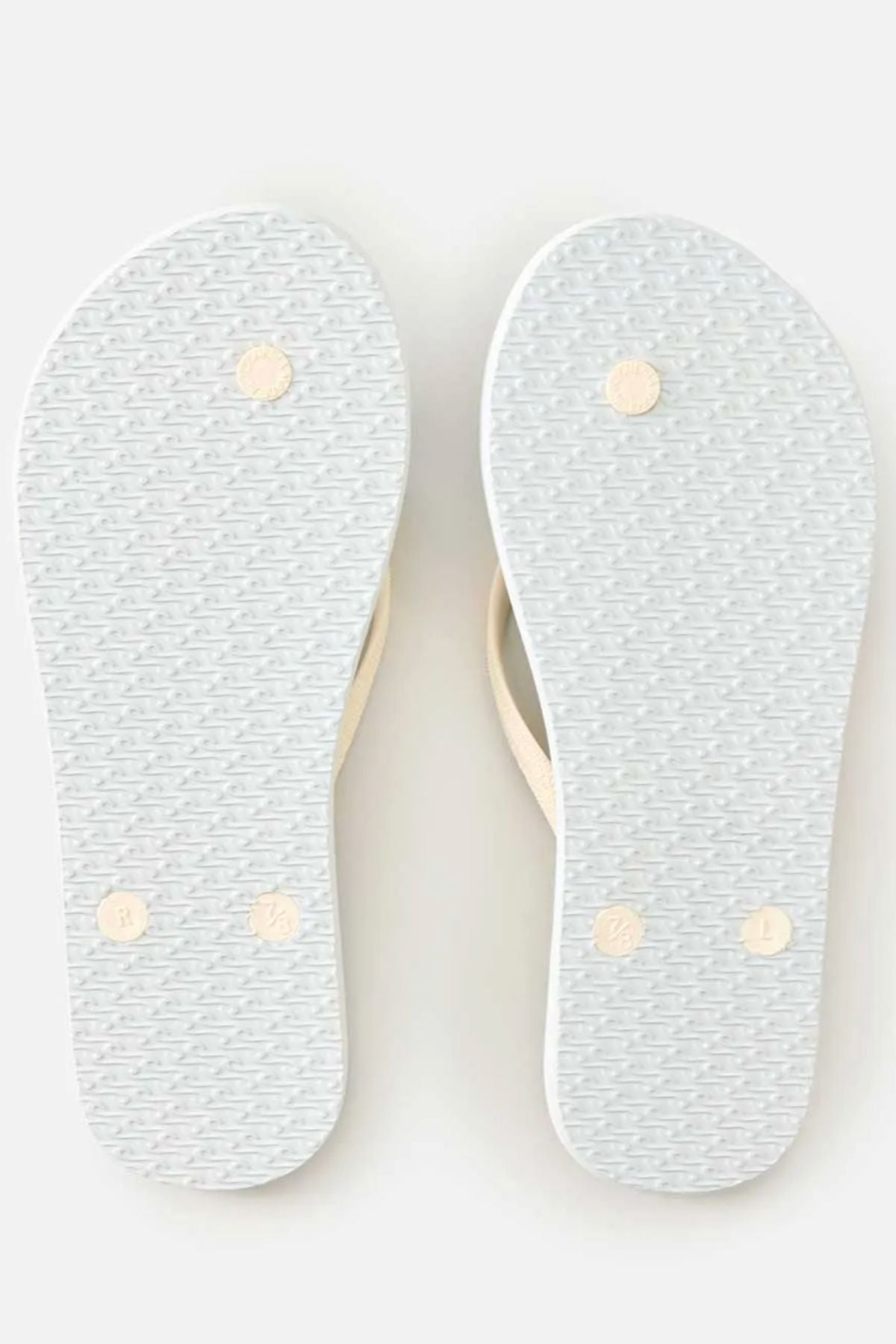 A pair of Rip Curl Mixed Bloom Thongs are shown from the bottom, featuring textured white rubber soles with four circular grip points on each and a classic 3-point design. The light-colored straps are barely visible from this angle.