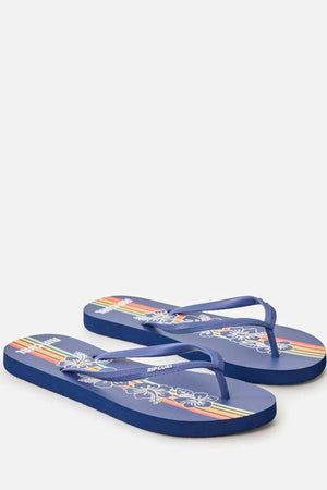 The Rip Curl Mixed Bloom Thongs feature blue straps, white floral designs, multicolored diagonal stripes on the footbed, an algae-blended EVA foam sole for comfort, and visible "Rip Curl" branding.