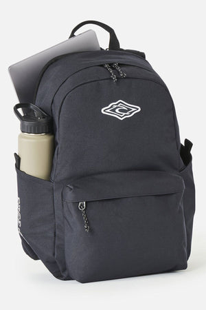 Rip Curl Crusher 30L Classic Backpack in black, featuring a front zip pocket, a water bottle in the side pocket, and a laptop stored in the main compartment.