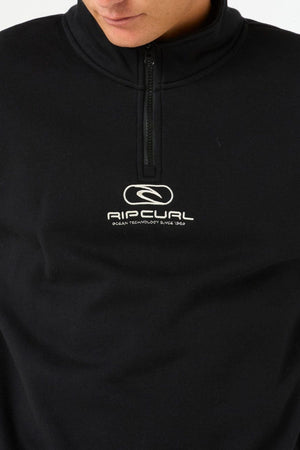 Close-up of a person in the Rip Curl Pill Icon 1/4 Zip Crew, a black Organic Cotton Poly Fleece sweatshirt with chest embroidery featuring the Rip Curl Pill Icon and "Ocean Technology Since 1969." Only part of the face is shown.