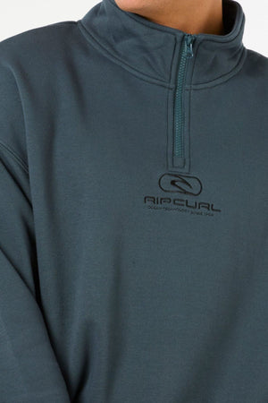 Someone wearing a teal Rip Curl Pill Icon 1/4 Zip Crew pullover with a high collar, made from Organic Cotton Poly Fleece. The chest displays the Rip Curl logo and "Ocean Technology Since 1969." The person’s face is mostly out of frame.