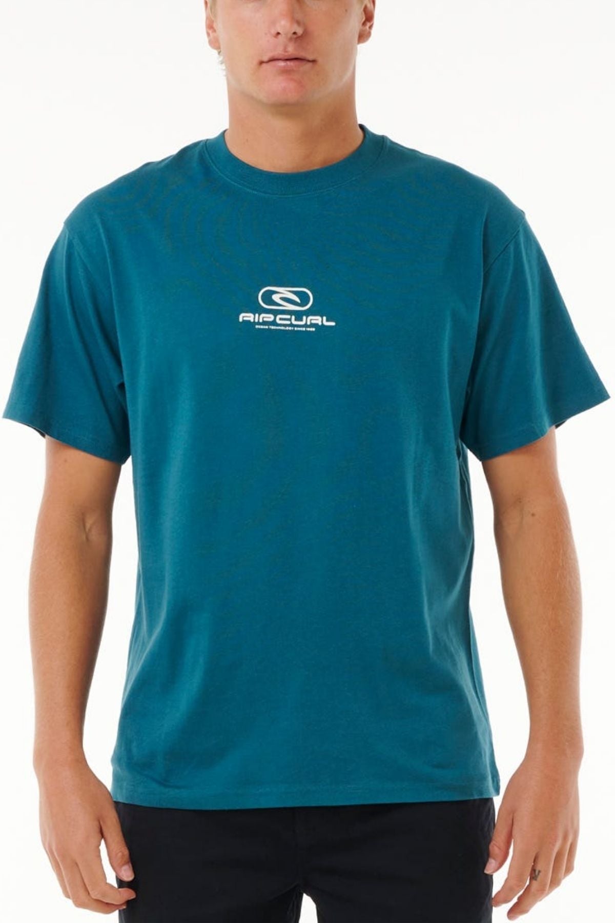 Someone stands against a plain white background wearing the Rip Curl Pill Icon Tee, made from 100% cotton and featuring the logo and text on the chest.