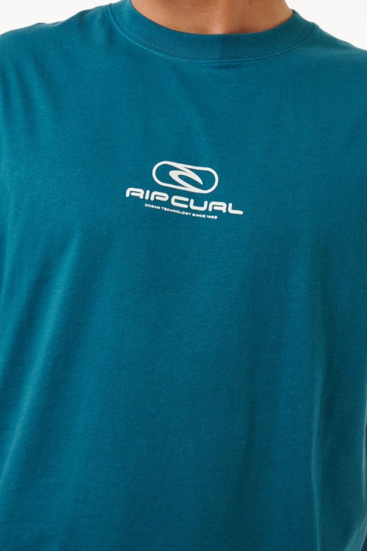 Someone in the Rip Curl Pill Icon Tee sports a 100% cotton shirt with the logo and "Ocean Technology Since 1969" printed in white on the teal chest.