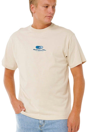 A man stands with one hand in his jeans pocket, looking to the side, wearing the Rip Curl Pill Icon Tee—a 100% cotton shirt featuring a small blue chest logo.