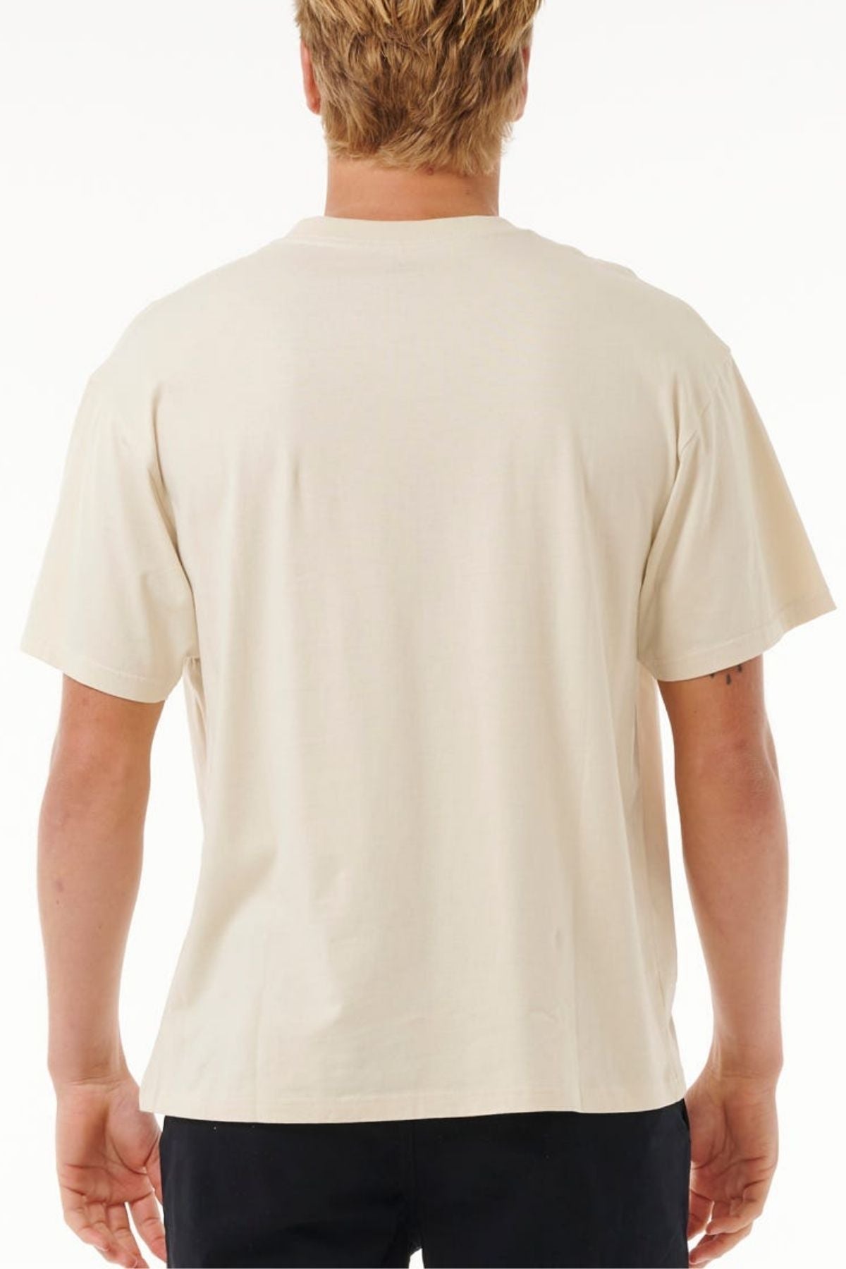 A person with short, light-colored hair is seen from the back wearing a Rip Curl Pill Icon Tee, made from 100% cotton, paired with dark pants against a white background.