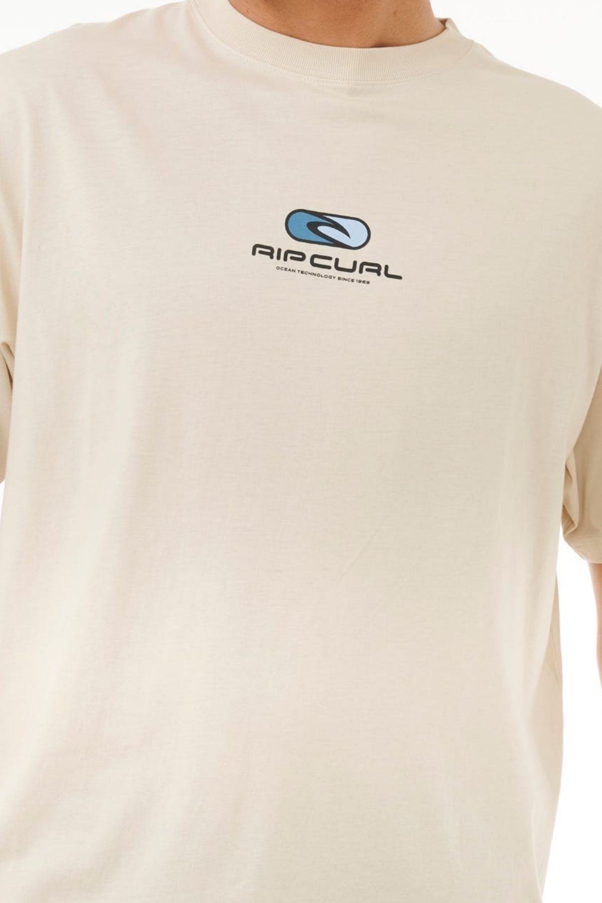 A person wearing a Rip Curl Pill Icon Tee, a classic 100% cotton shirt featuring "RIP CURL" with a stylized logo on the chest, against a plain light-colored background.