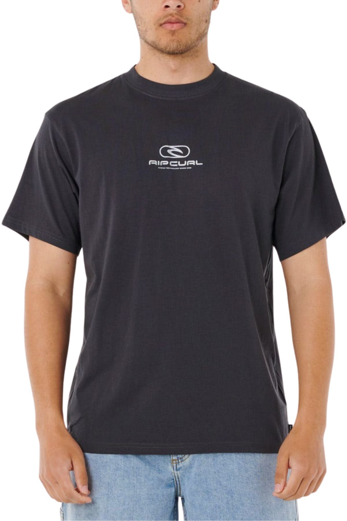 Someone wearing a Rip Curl Pill Icon Tee with a small white chest logo and text, made from 100% cotton, paired with light blue jeans, stands against a plain white background.