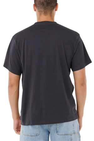 Someone stands with their back to the camera in a plain black Rip Curl Pill Icon Tee and light blue jeans, the relaxed fit of the t-shirt contrasting stylishly against a minimalist white background.