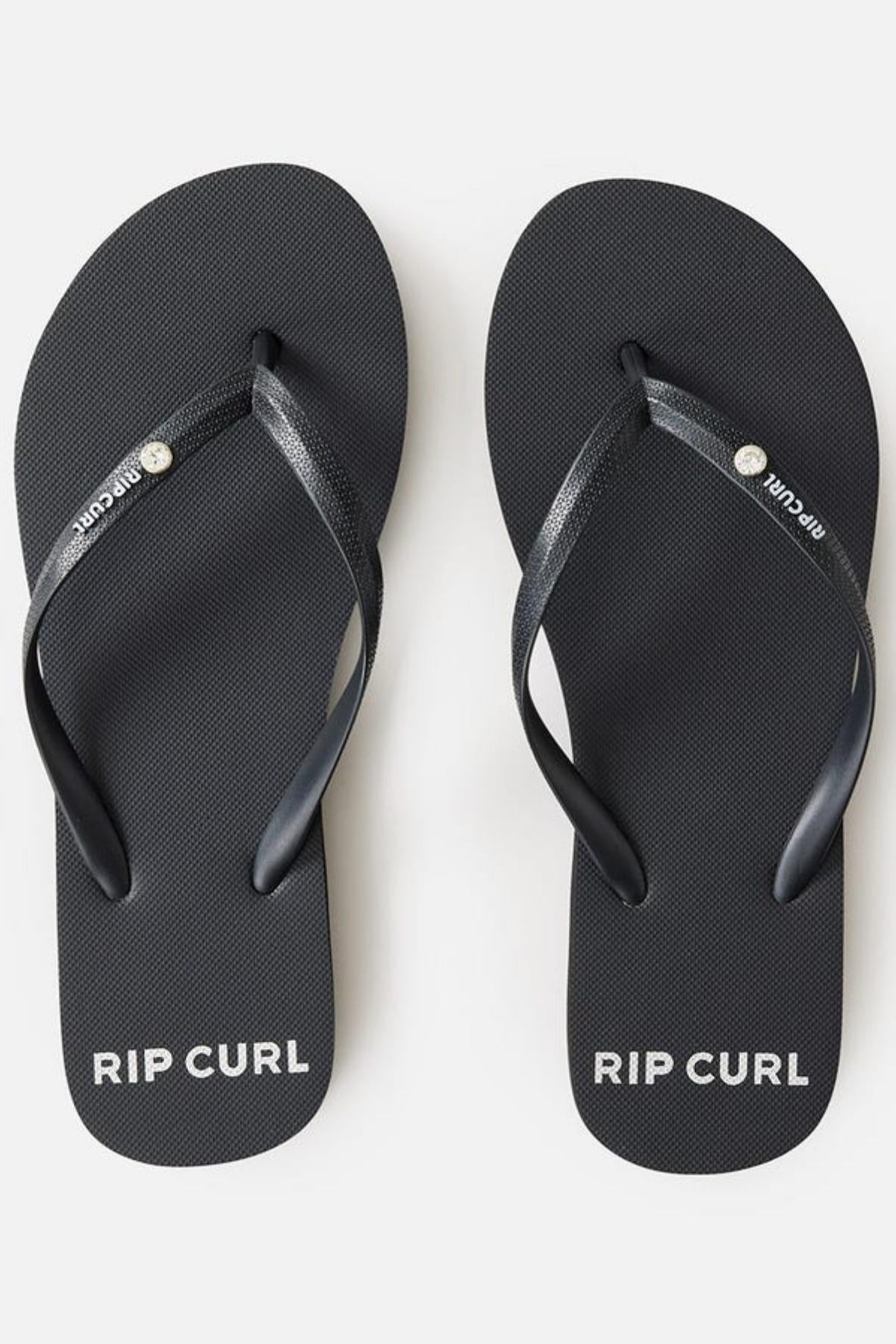 A pair of Rip Curl Premium Surf Bloom Thongs featuring black straps with a small metallic button that says "Rip Curl." The brand name "RIP CURL" is printed in white on the fine mesh-textured black footbeds near the toes.