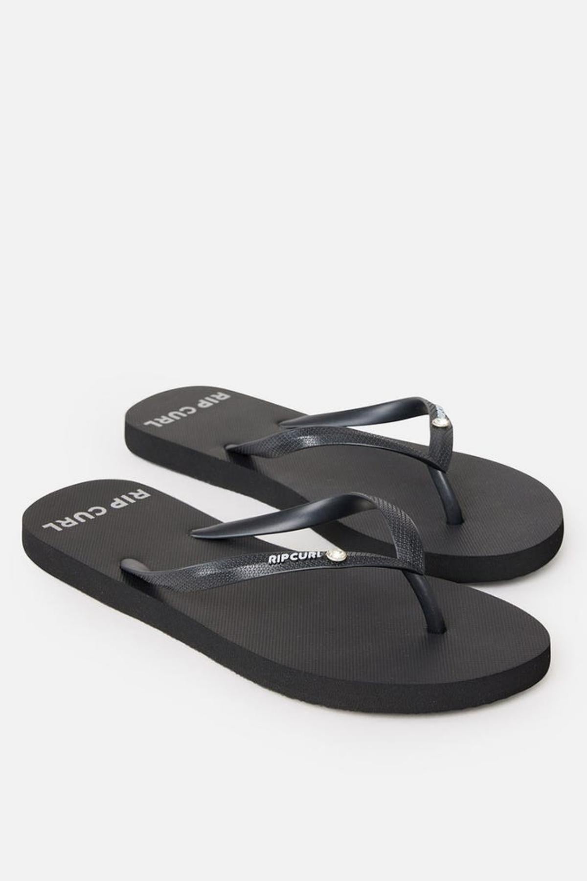 A pair of Rip Curl Premium Surf Bloom Thongs with a simple design, featuring the brand name "Rip Curl" printed in white on the straps and footbed. The black straps have a subtle texture, and the flip-flops have a plain rubber sole. The image is on a white background.