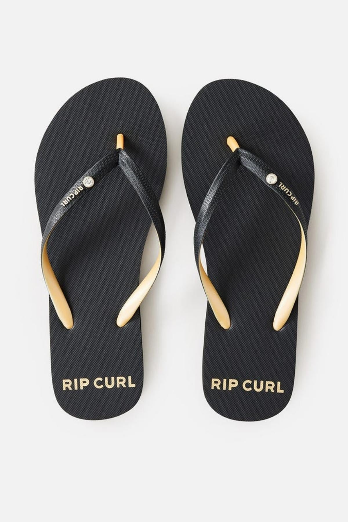 A pair of Rip Curl Premium Surf Bloom Thongs in black, featuring "RIP CURL" written in white on each footbed. The straps are black with a metallic silver button at the center, and the left strap also displays the brand name "RIP CURL" in white.