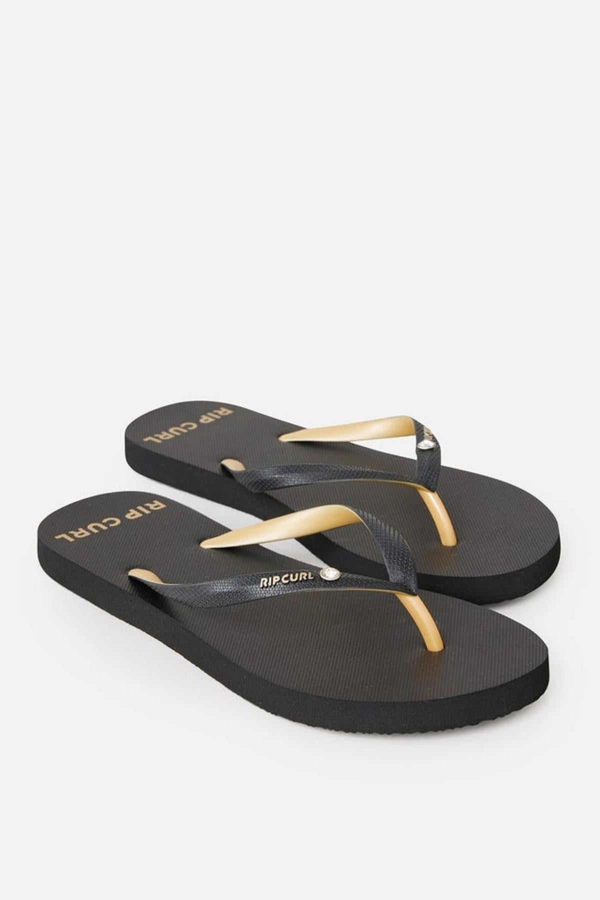 A pair of Rip Curl Premium Surf Bloom Thongs with a black textured sole and straps. The straps are black with a single beige stripe running through the center. The brand name "RIP CURL" is printed in white both on the footbed and on the strap. The flip-flops are displayed against a plain white background.
