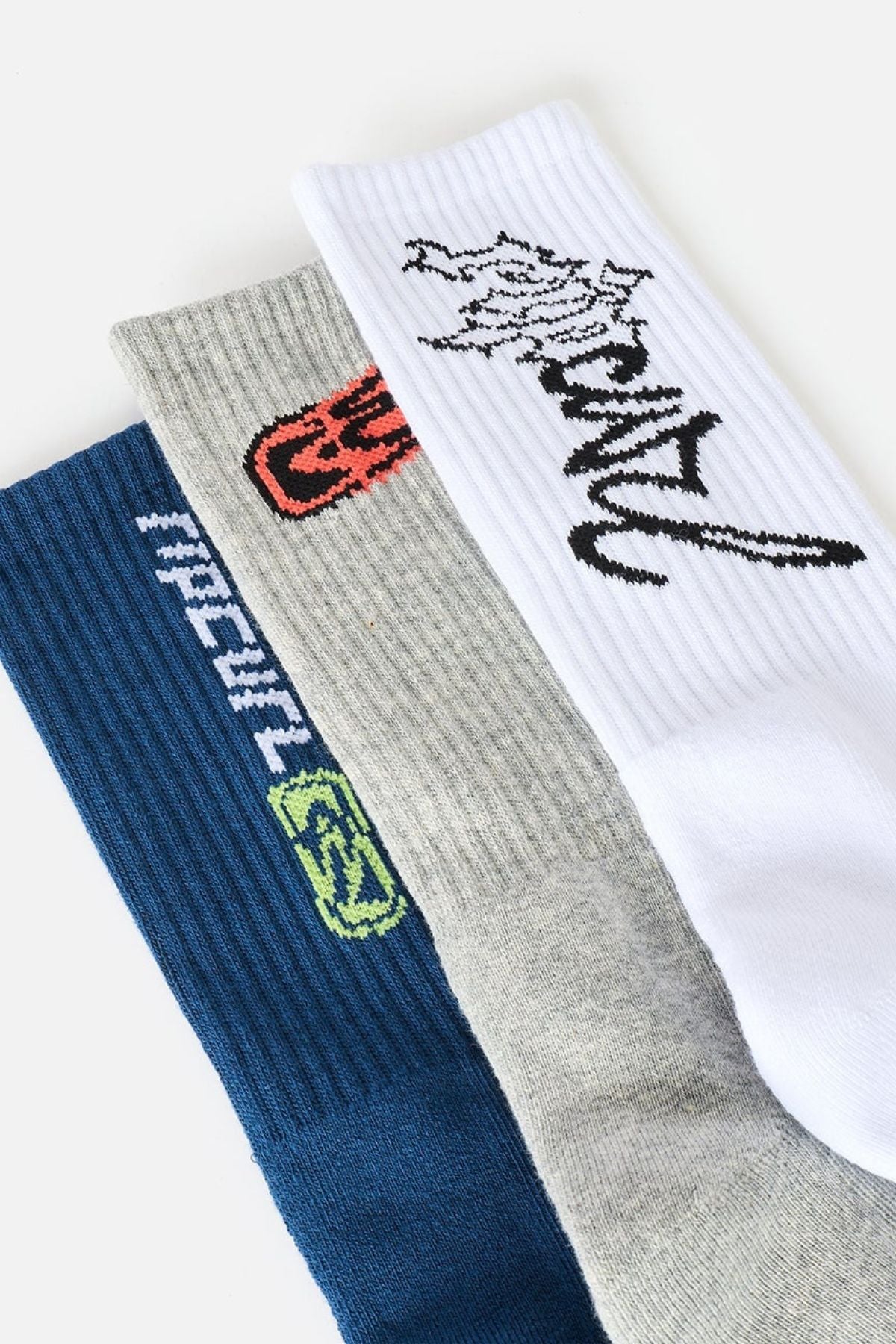 Three pairs from the Rip Curl Retro Crew Sock 3 Pack in blue, grey, and white, each featuring distinct text and graphic designs near the cuffs in various colors. These ribbed, cushioned socks are displayed overlapping on a light background, highlighting their comfort and stylish appeal.