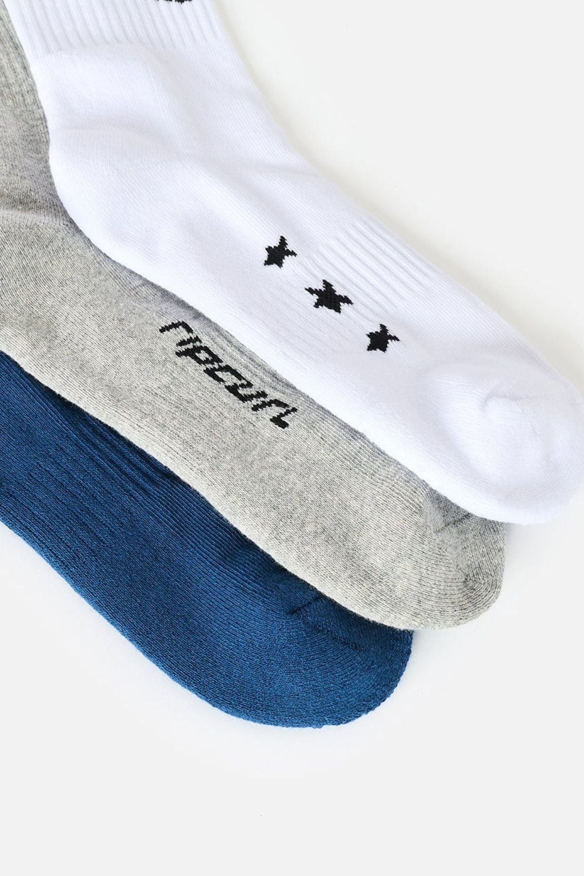Three pairs of socks from the Rip Curl Retro Crew Sock 3 Pack—featuring white with small black designs, heather gray with text, and solid blue—are layered side by side on a white background. These crew socks provide cushioned comfort and dependable arch support for everyday wear.