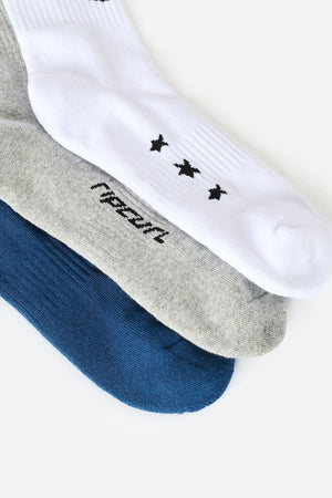 Three pairs of socks from the Rip Curl Retro Crew Sock 3 Pack—featuring white with small black designs, heather gray with text, and solid blue—are layered side by side on a white background. These crew socks provide cushioned comfort and dependable arch support for everyday wear.