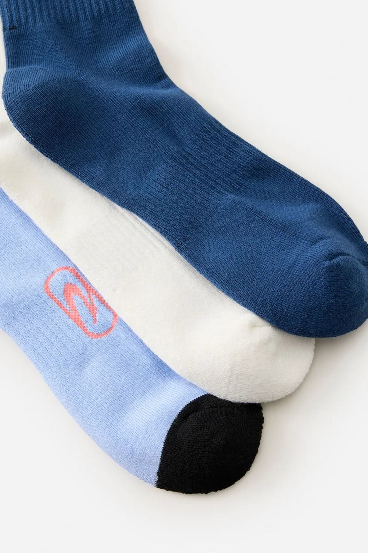 Three pairs of Rip Curl Retro Crew Socks—one solid dark blue, one white, and one light blue with a black toe and pink detail—are laid out overlapping on a light background. This 3-pack offers both comfort and style.