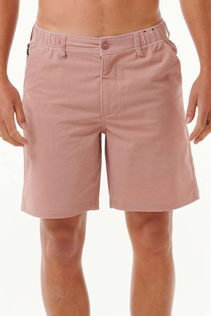 A person stands against a plain background, wearing Rip Curl Saltwater Culture Cord Boardwalk Shorts in pink. These shorts include belt loops, buttons, and side pockets, all incorporating quick-dry technology. The person's upper body is not shown.