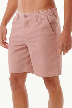 A person wearing Rip Curl Saltwater Culture Cord Boardwalk Shorts in light pink, showcasing an elastic waistband and side pockets. Designed with quick-dry technology, these shorts feature a front button and zipper, making them ideal for any beach stroll. The individual is posing against a plain white background.