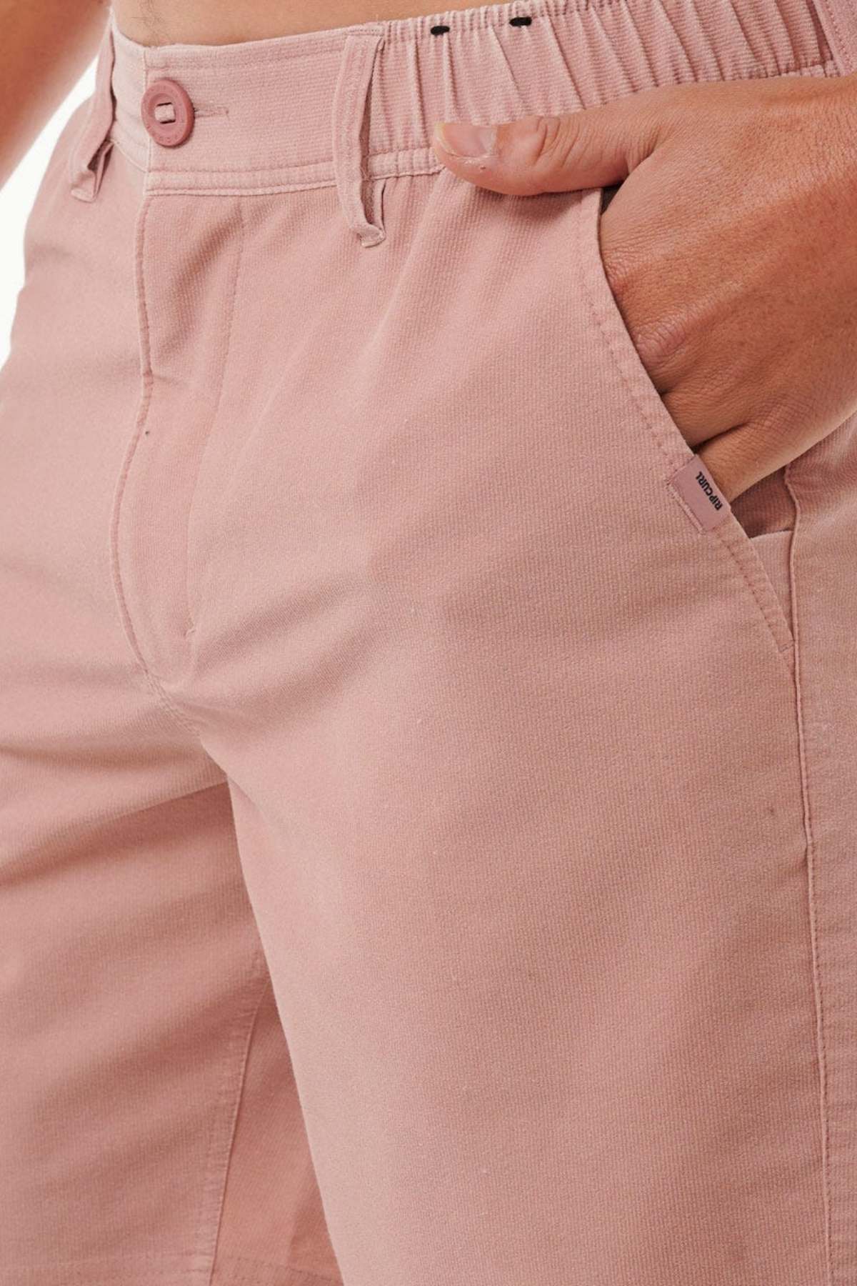 Close-up of a person wearing the Rip Curl Saltwater Culture Cord Boardwalk Short in pink, with one hand in the pocket. The fabric looks soft and subtly textured, equipped with quick-dry technology for added comfort. A button and zipper closure are evident, and the shorts boast a casual, relaxed fit, ideal for any laid-back day.