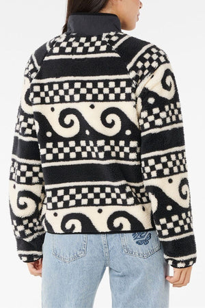 A person is seen from the back wearing the Rip Curl San Carlos Polar Fleece, featuring a black and white swirl and checkerboard pattern, paired with light blue jeans, against a white background.