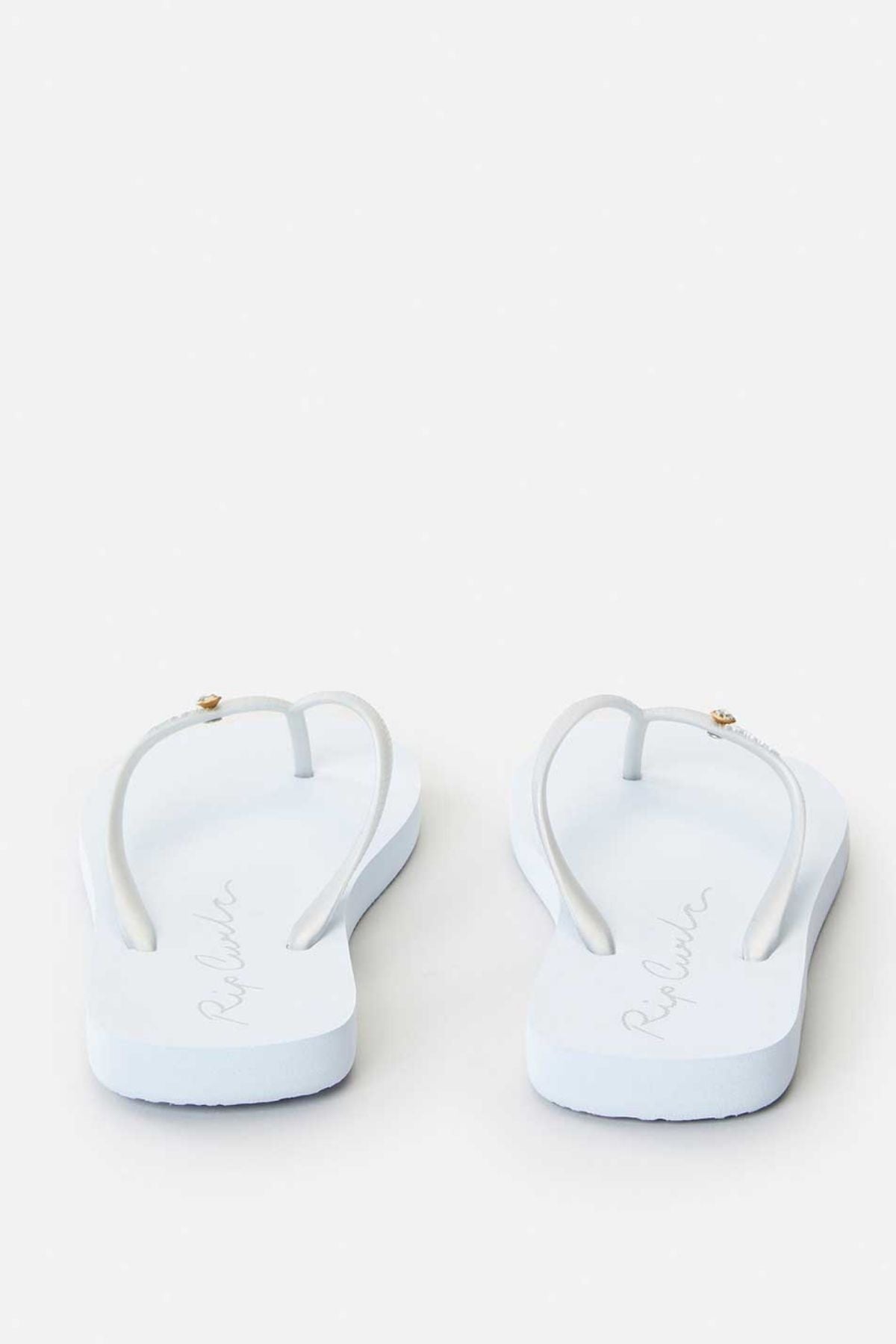 The Rip Curl Script Wave Bloom Thongs are displayed against a plain white background, showcasing their Zori construction. These white flip-flops feature thin straps adorned with a small decorative element on each, while the footbeds highlight a subtle signature design.