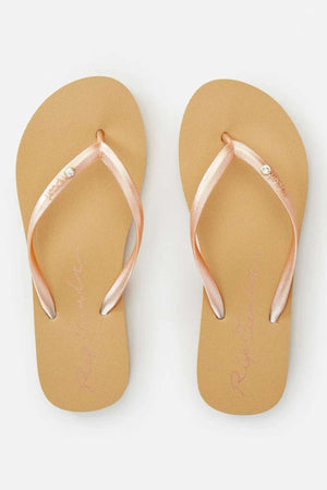 A pair of Rip Curl Script Wave Thongs in beige, adorned with pink metallic straps each embellished with a small decorative gem. The premium EVA footbed and ergonomic design guarantee comfort. These flip-flops are displayed side by side on a plain white background.