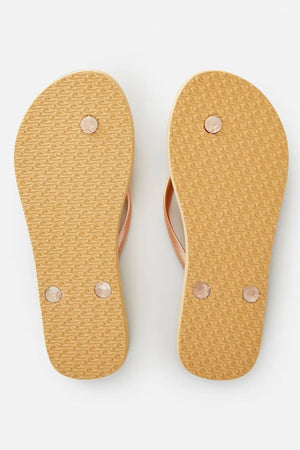 The image displays the underside of two tan Rip Curl Script Wave Thongs with a textured sole, highlighting their ergonomic design. Each sole features three round rubber grips for enhanced traction, and the straps are in a light shade.