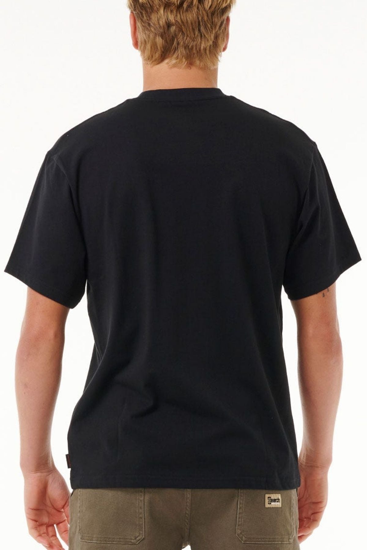 A person with short, light brown hair is shown from the back, wearing a plain black Rip Curl Search Embroidery Tee (100% cotton) and olive green pants with a small label on the back pocket, standing against a white background.