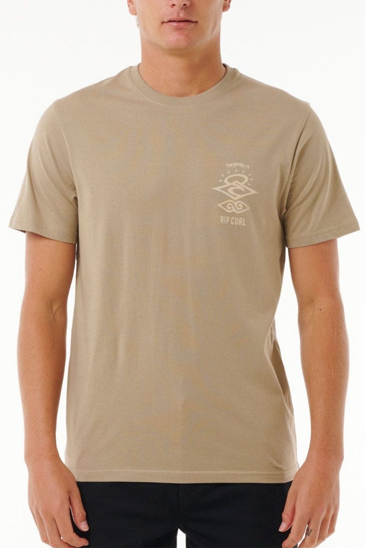 A person stands against a plain background wearing a beige Rip Curl Search Icon Tee, crafted from organic cotton with a subtle logo on the chest, paired with black pants.
