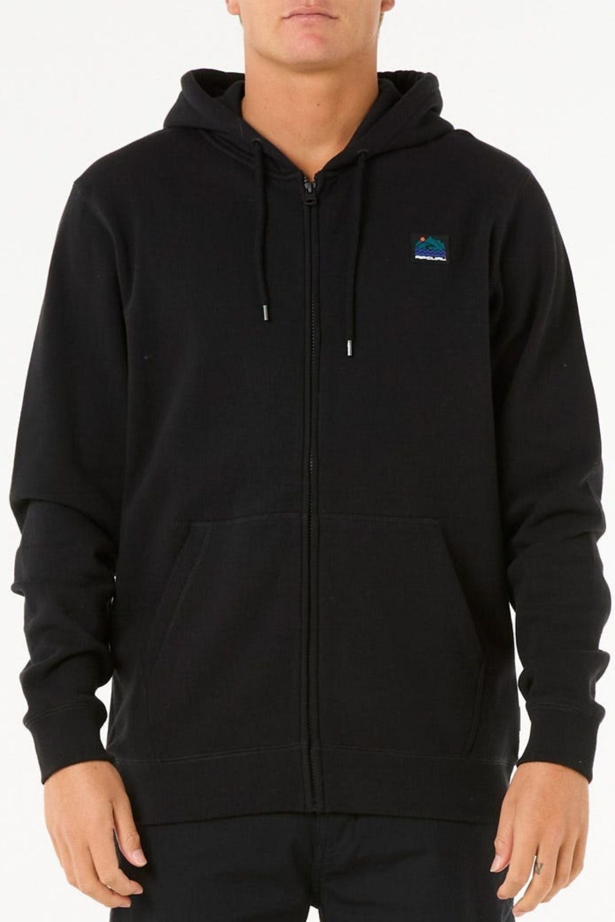 A person wears a Rip Curl Search Zip Thru Hood—plain black, cotton polyester blend, standard fit, with a small colorful rectangular patch on the left chest—standing against a white background.