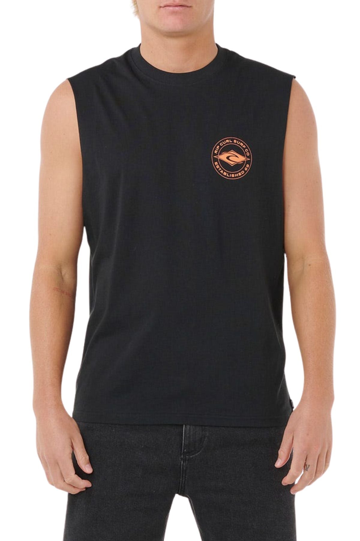 A person wearing a sleeveless black Rip Curl Staple Muscle shirt with a small round orange and black logo on the left chest, paired with black jeans, stands against a white background.