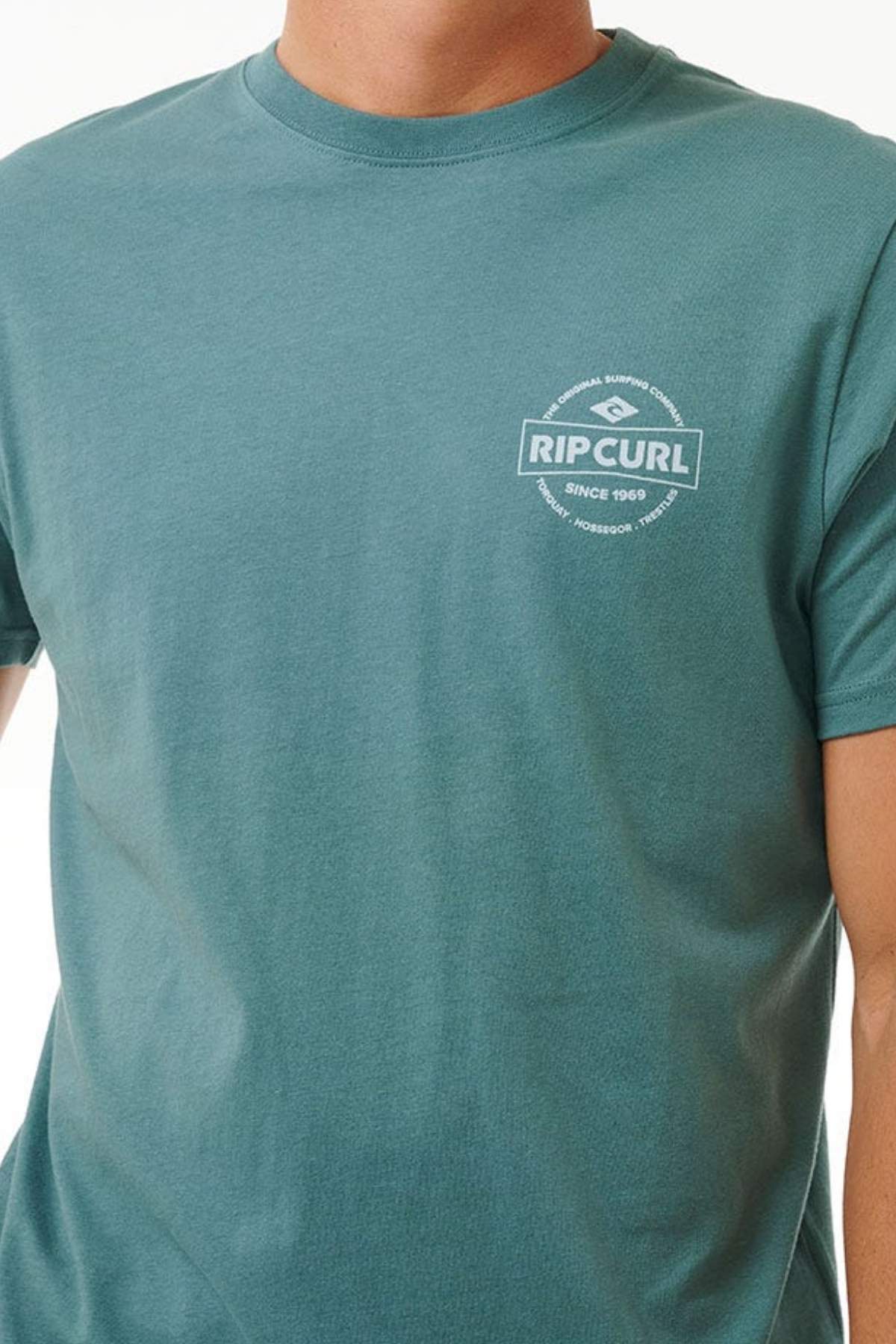 A person wears a teal Rip Curl Staple Tee made from soft cotton jersey, with a small white logo and "RIP CURL SINCE 1969" on the left chest. Only the upper torso is visible; the face is not shown.