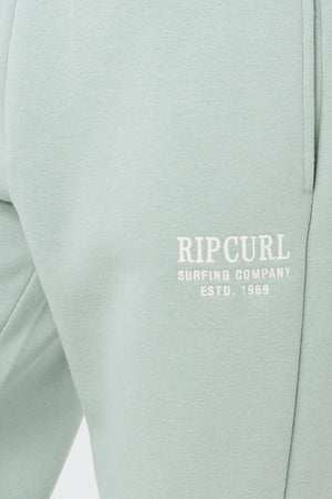 Close-up of light green Rip Curl Surf Staple Trackpant with a pocket and white "RIP CURL SURFING COMPANY ESTD. 1969" text on the upper thigh—ideal, comfy loungewear for a relaxed day.