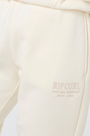 Close-up of Rip Curl Surf Staple Trackpant in cream with "Rip Curl Surfing Company Estd. 1969" logo embroidered by the pocket. Soft, slightly textured fabric offers comfort and a classic surf-inspired style for everyday wear.
