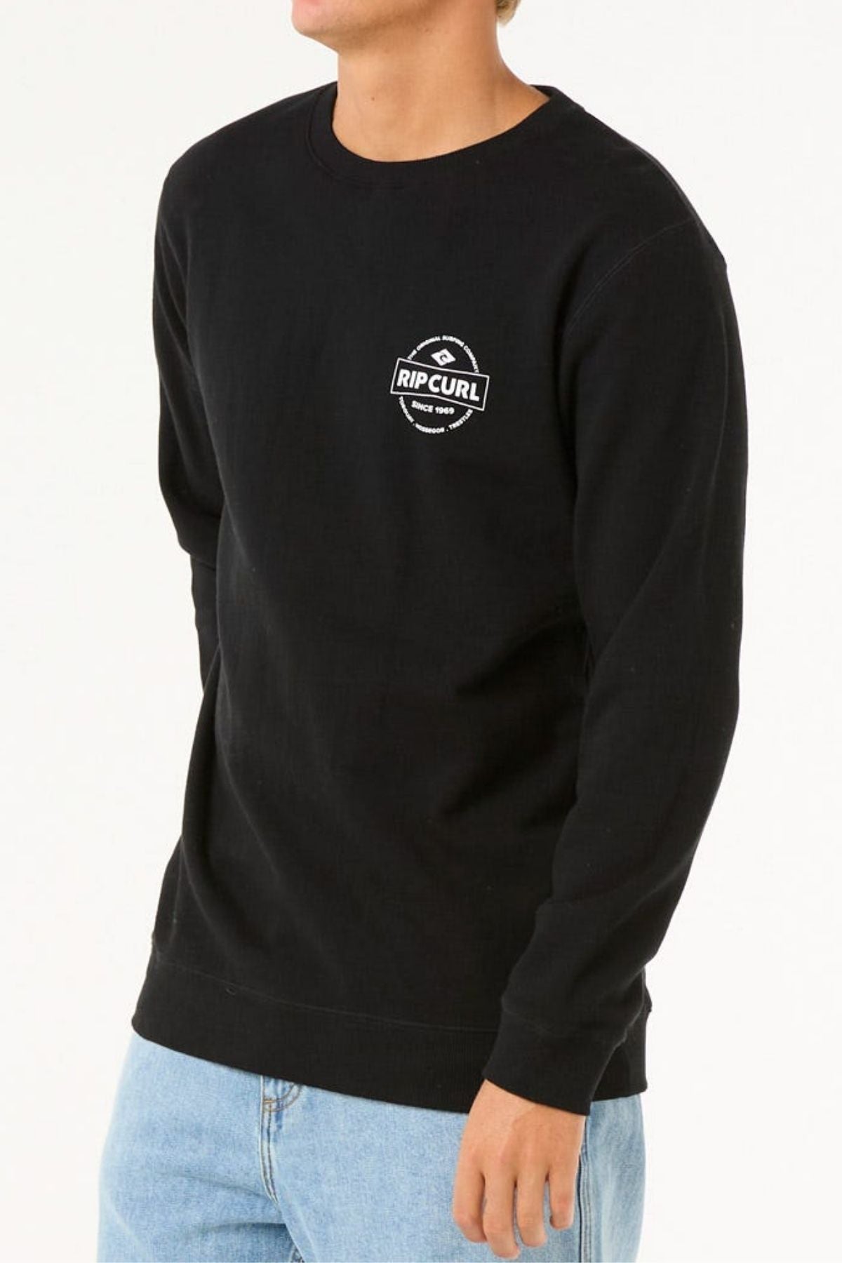 Wearing the Rip Curl Stapler Crew black sweatshirt, crafted from soft cotton-polyester fleece with a small white chest logo, paired with light blue jeans against a plain white background.