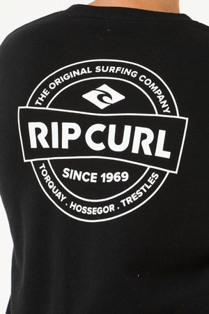 The Rip Curl Stapler Crew in black features a bold white "RIP CURL" logo on the back, surrounded by "The Original Surfing Company," "Since 1969," and the locations "Torquay," "Hossegor," and "Trestles.