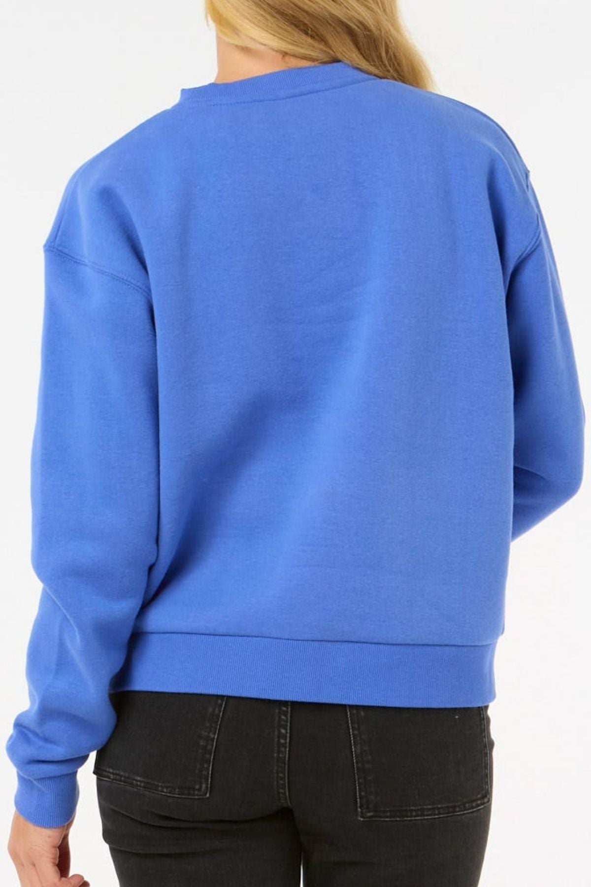 A person with long blonde hair, shown from the back against a plain light background, is wearing the Rip Curl Surf Staple Relaxed Crew in bright blue with black jeans.