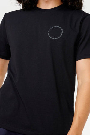 A person wearing a Rip Curl Vaporcool Search Rubix Tee, featuring a small circular text pattern on the front. The quick-dry fabric ensures comfort, and the moisture-wicking design keeps you fresh. The background is plain and light-colored.