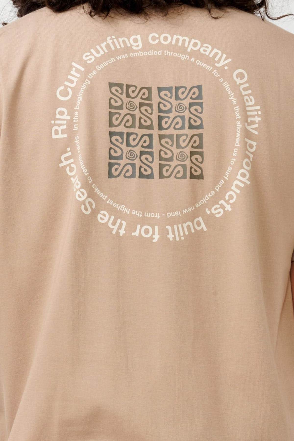 The Rip Curl Vaporcool Search Rubix Tee is a beige shirt that showcases a circular design on the back with abstract patterns at its center and text around it, stating "Rip Curl surfing company. Quality products built for the search." Made with VaporCool technology, it offers moisture-wicking and odor control to keep you fresh.