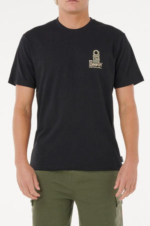 A person wears a black Rip Curl Vaporcool Search Stack Tee with a small tan graphic and text on the left chest, known for quick drying and moisture control, paired with olive green pants, standing against a plain white background.