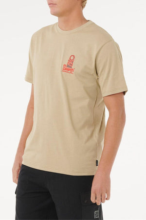 A person in a beige Rip Curl Vaporcool Search Stack Tee with odour control and a small red graphic and text on the chest, paired with black pants, stands against a plain white background.