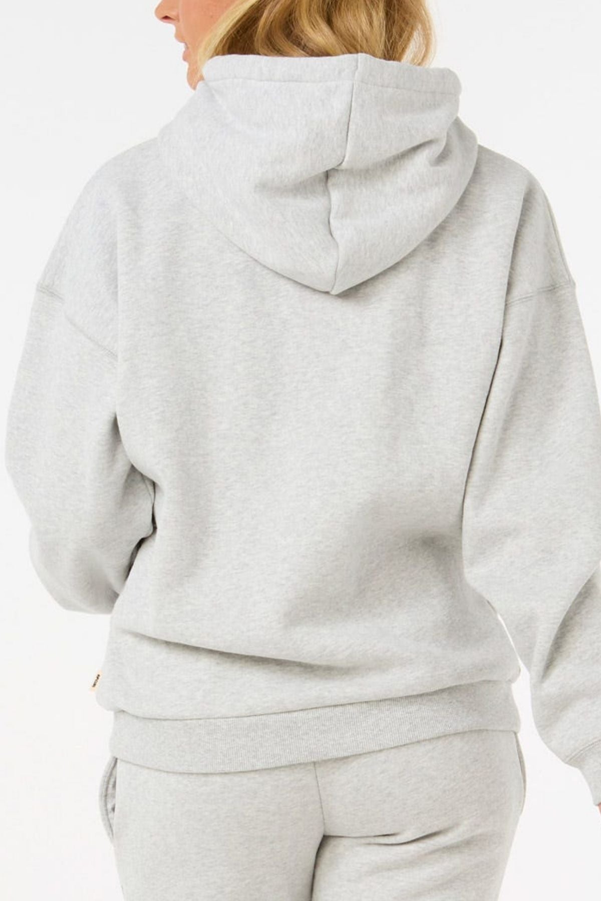 A person with blonde hair is shown from the back against a plain white background wearing a light gray Rip Curl Varsity Hoodie made from Cotton Poly Fleece with an adjustable drawcord, paired with matching sweatpants.