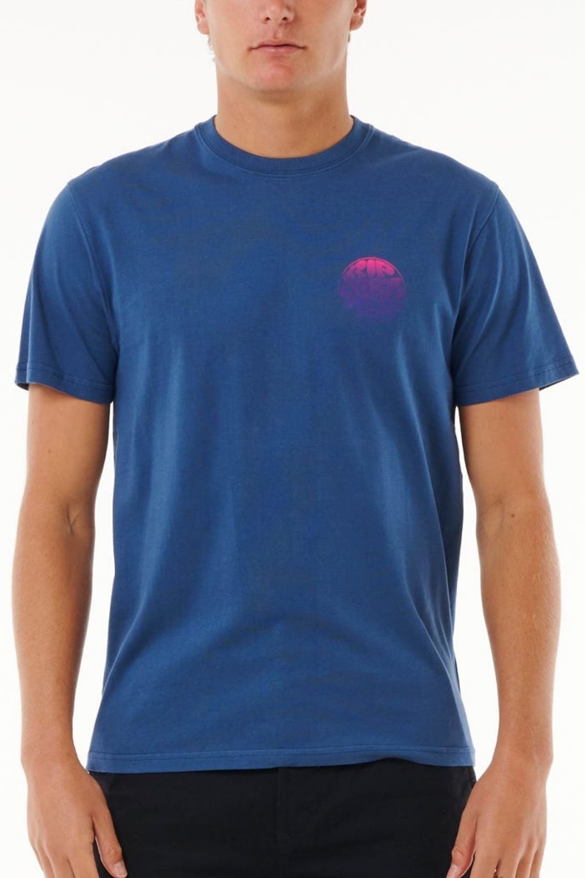 Wearing the Rip Curl Wetsuit Icon Tee—blue cotton with a crew neck and small pink circular logo on the left chest—a person stands against a plain white background.