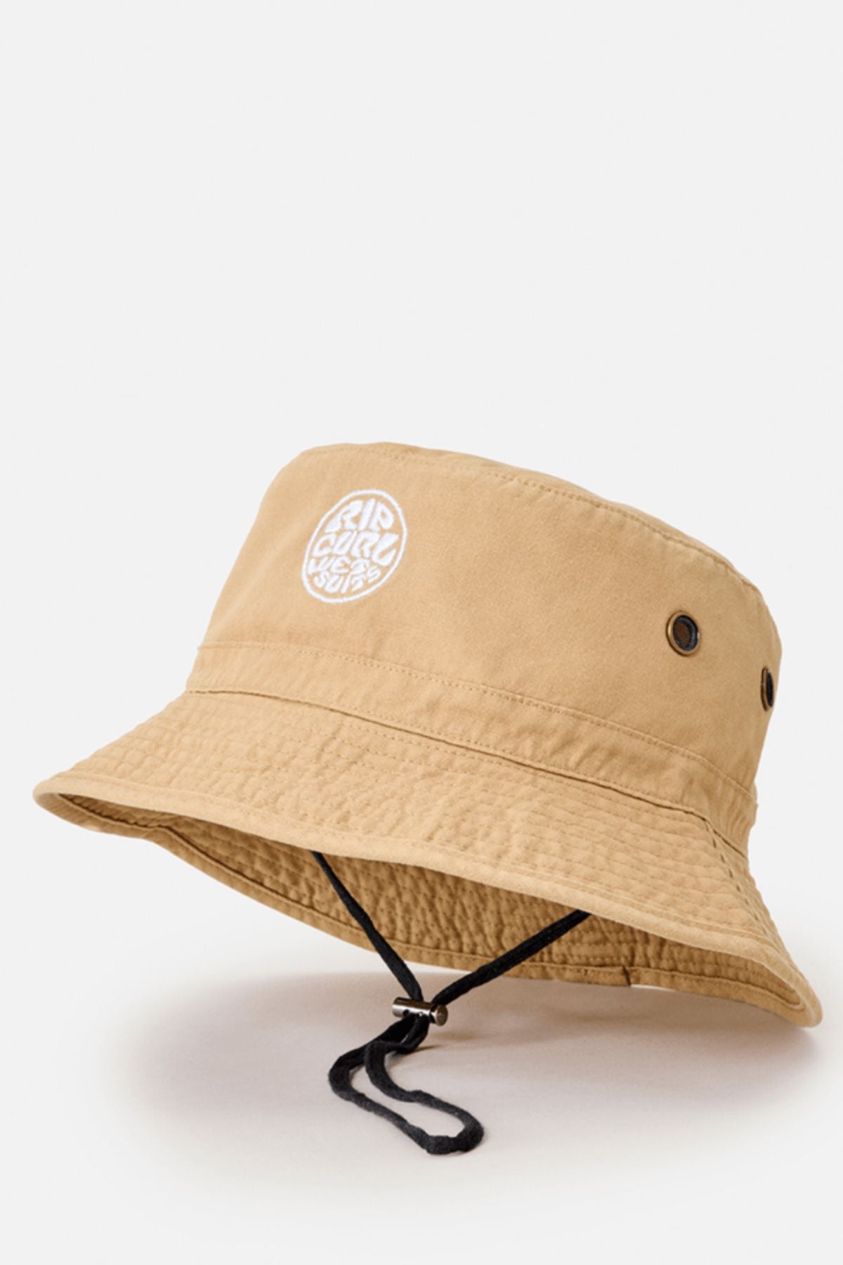 The Rip Curl Wetty Icon Bucket Hat is tan, made from organic canvas, and features a white embroidered circular logo on the front, two side eyelets, and an adjustable black chin strap. Displayed against a plain white background.