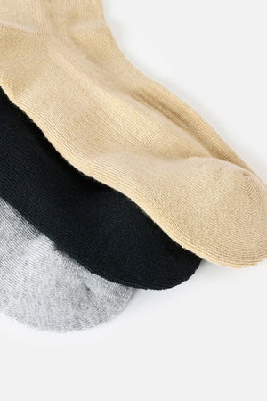 Three pairs of Rip Curl Wetty Crew Socks in beige, black, and light gray are stacked on a white background, each pair partially overlapping the next. The socks feature moisture-wicking technology for all-day comfort and built-in arch support to help keep your feet feeling their best.