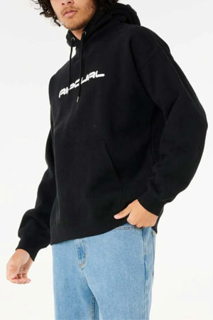 A person wearing the Rip Curl Dosed Up Hood—a black cotton polyester fleece hoodie with white chest text—and light blue jeans stands against a plain light background. Their face is partially visible, with one hand in the hoodie pocket.