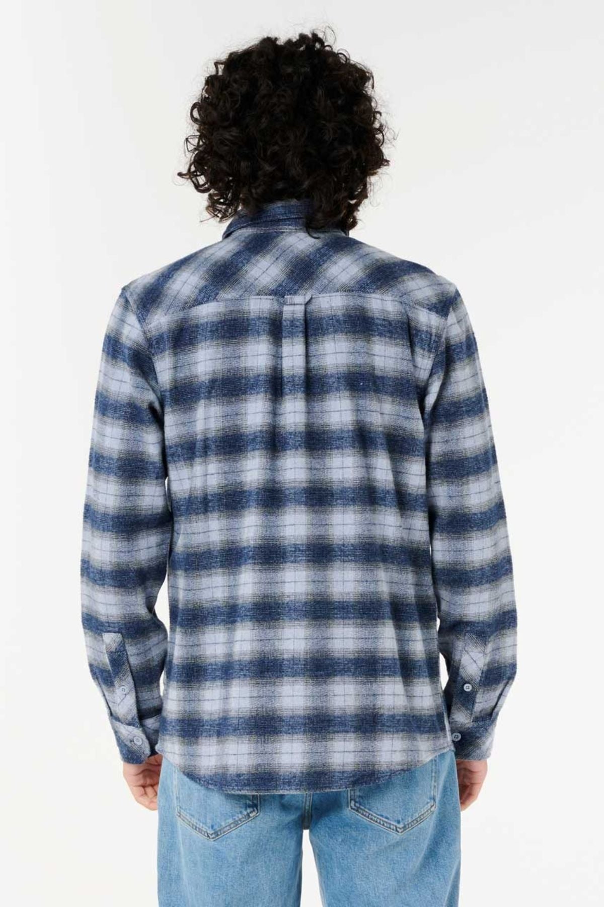 Seen from behind, a person with curly hair wears the Rip Curl Grinners Flannel Shirt in blue and white plaid and light blue jeans, standing against a plain white background.