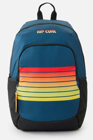 The Rip Curl Ozone Cool 30L Backpack is a blue school bag with a front pocket in red, orange, and yellow gradient stripes, black side pockets, and a black top handle. Made from recycled polyester.