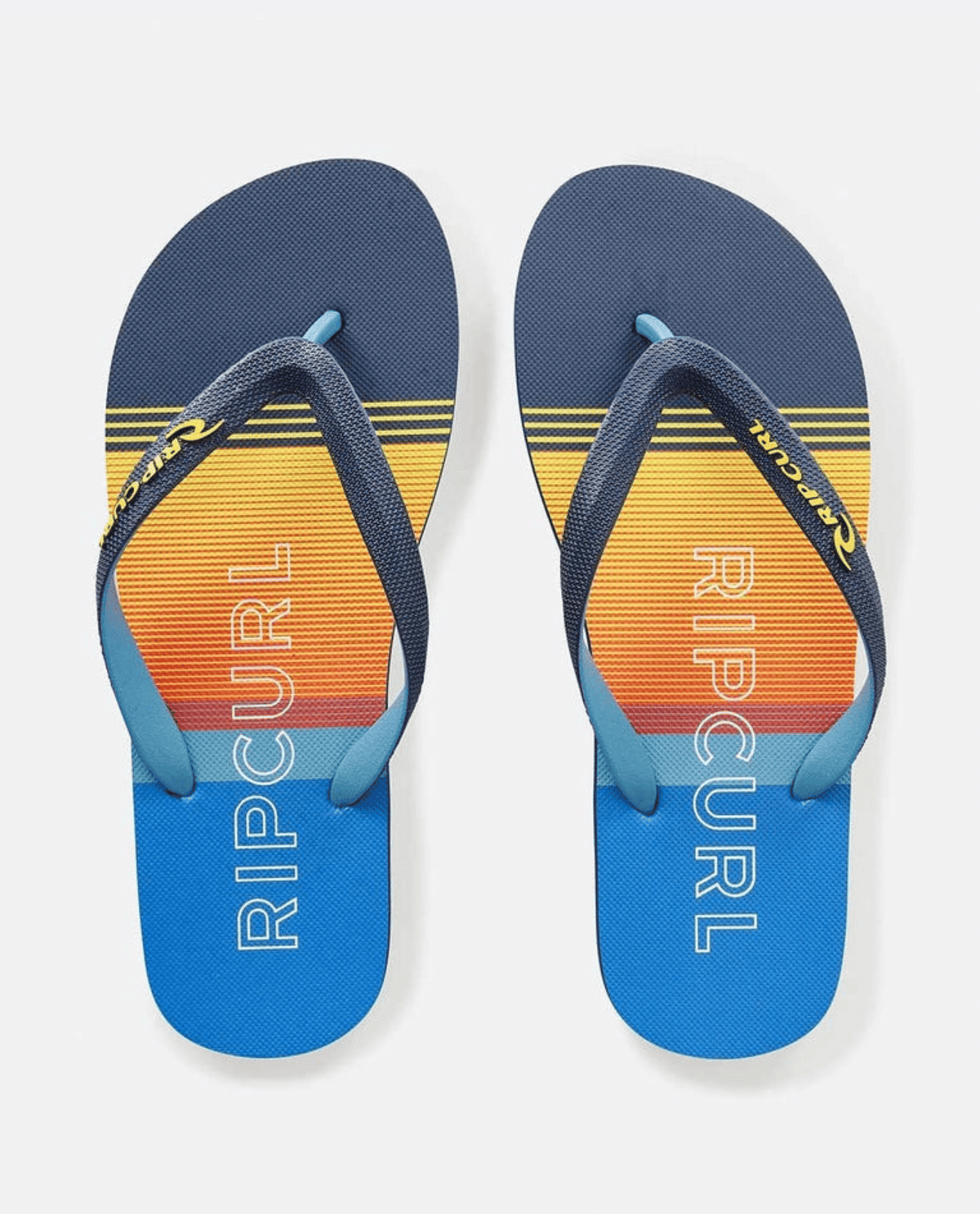 The Rip Curl Breakers Bloom Thongs feature a blue and orange gradient with "Rip Curl" on the soles and dark blue straps adorned with a logo. Made from BLOOM algae-blended foam, they offer eco-friendly fashion that's both stylish and sustainable.
